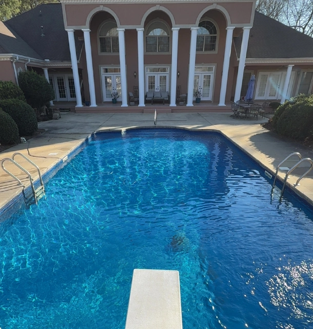 rectangular pool with diving board beside a large brick colonial home
